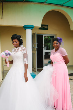 A Nigerian Bride and her Maid of Honour stand waiting outside a hotel.