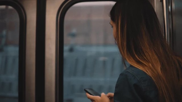 Beautiful woman taking a subway in Chicago, USA. Attractive female using smartphone while train is moving on sunset.
