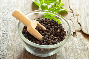 Black pepper corns in glass bowl with wooden scoop