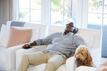 African American Senior man listening to music on a smart phone sitting on the couch at home