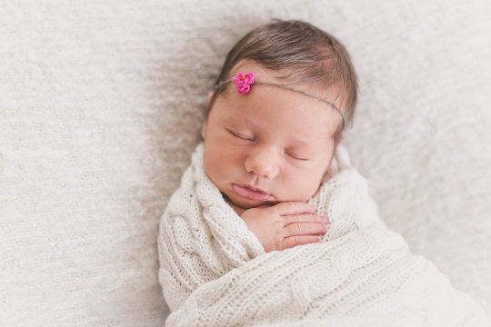 Sleeping newborn baby girl swaddled tightly in a knit blanket wearing a cute headband