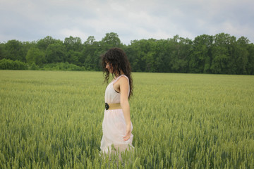Fototapeta na wymiar Woman Female Model in a Wheat Field Surrounded by Trees in Spring or Summer Wearing a Pink Flowing Dress