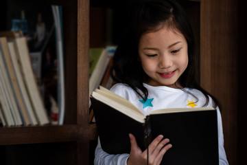 cute girl smiled and standing reading book in the library, children concept, education concept