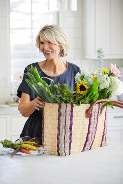 Senior woman in kitchen with farmers market basket with vegetables and flowers