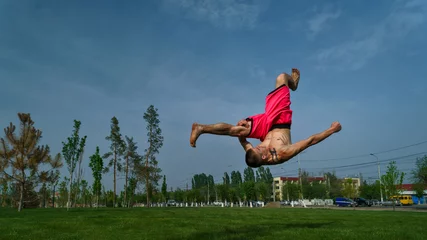 Photo sur Aluminium Arts martiaux Tricking on lawn in park. Man does somersault ahead. Martial arts and parkour. Street workout.
