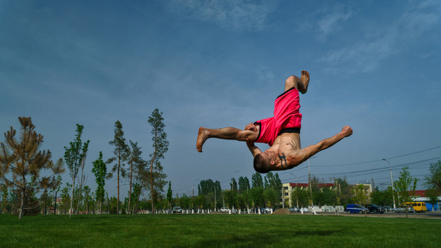 Tricking on lawn in park. Man does somersault ahead. Martial arts and parkour. Street workout.