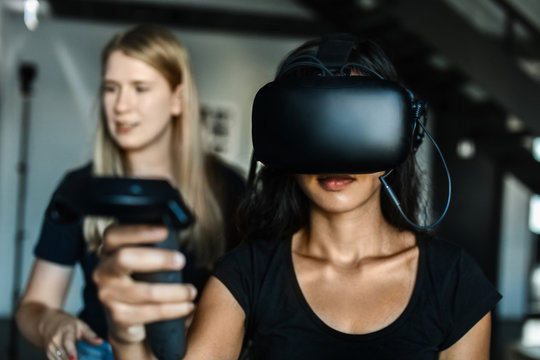 Caucasian young woman helps South-East asian girl putting on VR and controllers