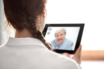 Rückenansicht einer Ärztin mit Tablet, Patientin im Live Chat, Telemedizin und Sprechstunde