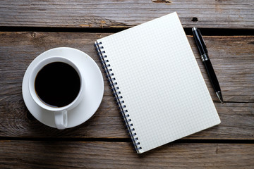 Notebook, pen and a cup of coffee on wooden table. 