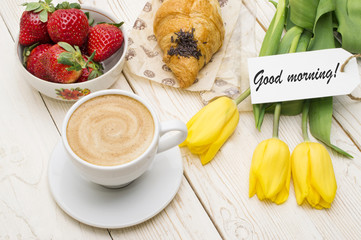 Cup of coffee, tulips, croissant, strawberries and Good morning massage on wooden background