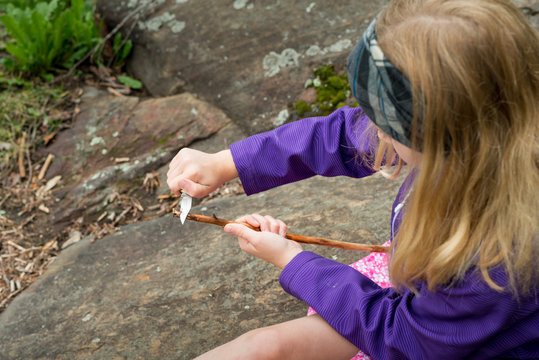 Girl Sharpening a Stick With a Knife While on Backcountry Wilderness Camping Canoe Trip