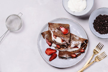 Homemade chocolate crepes with strawberry and cream on grey concrete background. Delicious breakfast. Selective focus