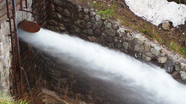Water discharge from the dam of the Lake Fregabolgia an Alpine artificial lake. Italian Alps. Italy. The water flows rapidly and splashes onto the ground