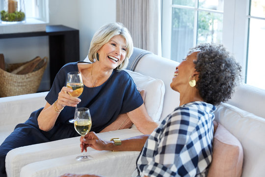 Senior women friends talking and drinking wine in living room at home