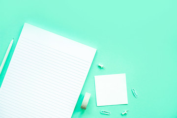 Beautiful office stationery flatlay with ruled notebook, pen, sticky note and paper clip on the bright desk with turquoise background.