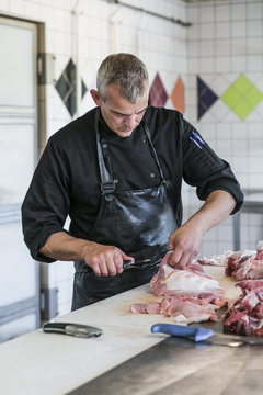 Man working as butcher cutting pieces of raw meat
