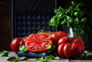 Big red tomatoes with green basil leaves on the old wooden background, selective focus