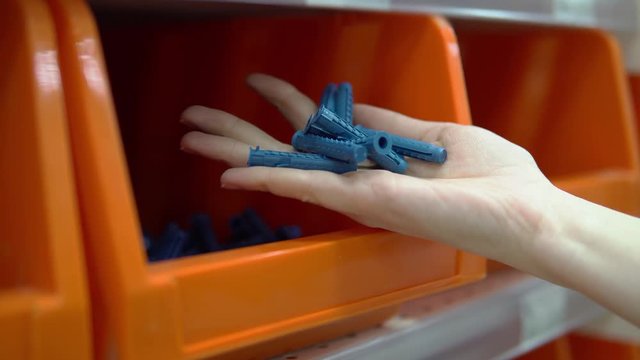 Close-up of a hand takes an orange container from a corrugated plastic plugs. Selection and purchase of building materials in the hypermarket.