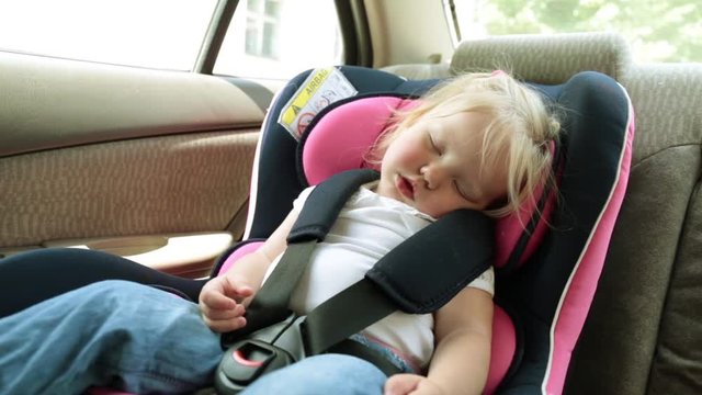 A small child sleeps in a car seat in the car.