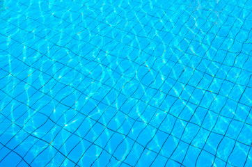 Tiled bottom of pool under transparent blue water with patches of sunlight