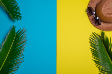 Fototapeta na wymiar Flat lay palm leaves, hat and sunglasses on blue and yellow background