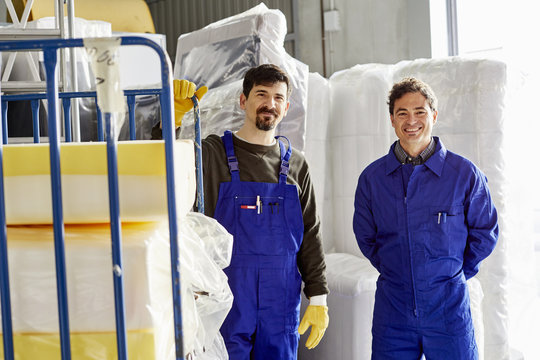 Confident Workers Standing By Mattress Packages At Sofa Workshop