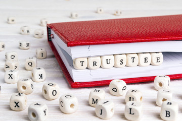 Word Trustee written in wooden blocks in red notebook on white wooden table.