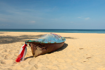 A small wooden fishing boat is lying on an empty beach.