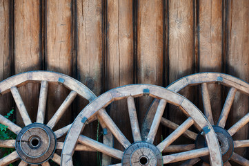three old wooden wheels from carts on a log wall background