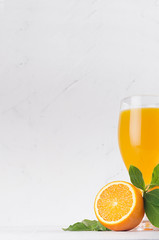 Fresh orange juice with slices oranges  and young green leaves closeup on soft light plaster background, vertical.