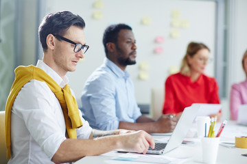 People in colored casual clothes using laptop and listening at job with white blackboard on background