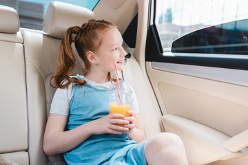 cheerful kid with juice looking out car window while sitting in car