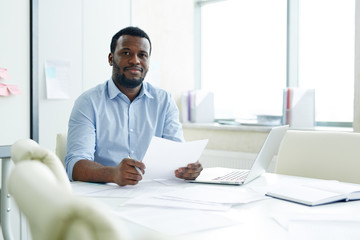 Obraz premium African-american businessman in elegant clothes with documents in hands looking at camera in working space