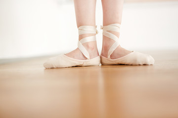 Women legs in ballet shoes champagne color making dance on floor on parquet 