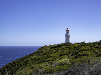 Fototapeta na wymiar lighthouse overlooking the ocean below on top of a green coastal cliff with a blue sky