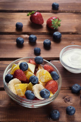Fruit salad from glass plate on dark wooden, style Rustic. Mix of strawberry , blueberry,banana and orange.