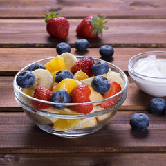 Fruit salad from glass plate on dark wooden, style Rustic. Mix of strawberry , blueberry,banana and orange.