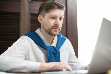 Obraz premium Concentrated man in elegant outfit sitting at cafe table and browsing data on laptop. 