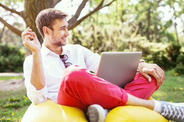 Fototapeta premium Making money online. Cheerful stylish man sitting in the open air and holding a coin