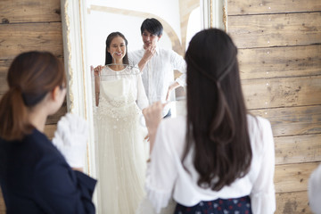 鏡越しにドレスを当てた姿を見る夫婦とプランナー
