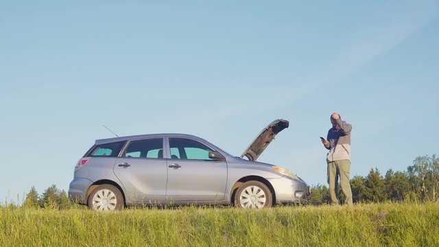 Young man on his phone as he checks what's wrong his broken down vehicle
