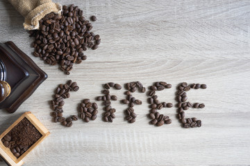 top view Coffee beans on wooden background in form of word of "coffee", grinder and sack in background