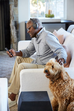 African American Senior man listening to music on a smart phone sitting on the couch at home
