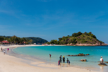 Tourists, adults and children are enjoying their leisure time at the beautiful white sandy Long Beach (Pasir Panjang) with its crystal clear turquoise blue water on Redang Island, Malaysia.