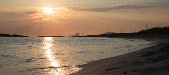  The sun shines through the clouds in the sky and reflects a beautiful light on the water and the beach.