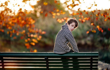 Boy perched on the back of a park bench in a park in autumn