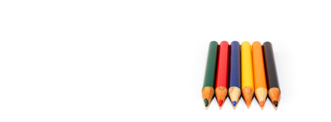 Coloured small pencils in colours green, red, blue, yellow, orange and black, aligned side by side in a closeup macro photo isolated on a seamless white background with large copy space for text.