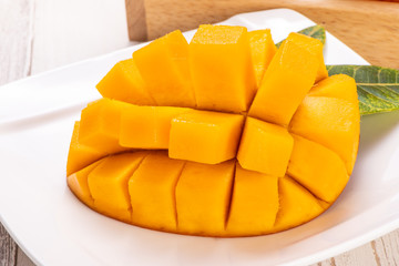 Fresh and beautiful mango in a white plate with sliced diced mango chunks isolated with   light wooden background, copy space(text space), blank for text