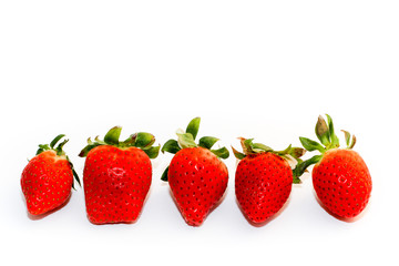Five fresh and natural red strawberries of different shapes with green leaves, side by side, isolated on a seamless white background.