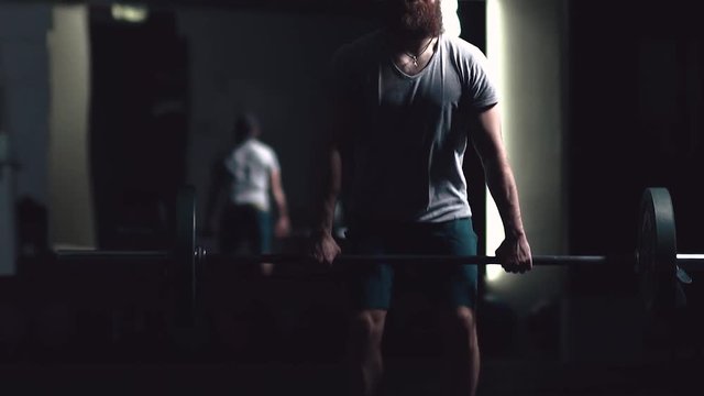 Sport in slowmotion. Brutal man with a beard is engaged in weightlifting in a dark room and performs the taking of the bar on his chest. Crossfit, weightlifting. The man is focused